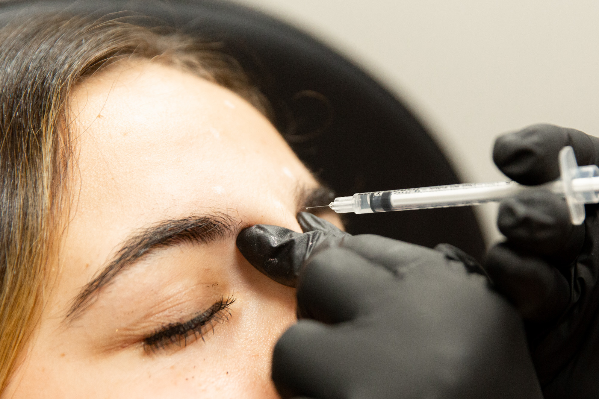 Marcos Medical provider holds Botox shot just above female client's skin between her eyebrows.
