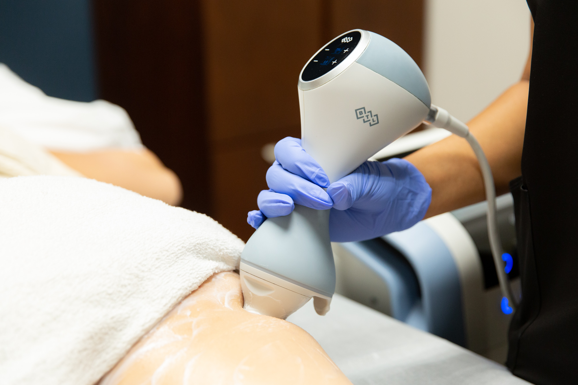 A Marcos Medical provider uses the Emtone application tool on a patch of bare skin on a patient's body. The tool is used by gently pressing down on the patient's skin. Very little skin can be seen, the rest is covered by towel.