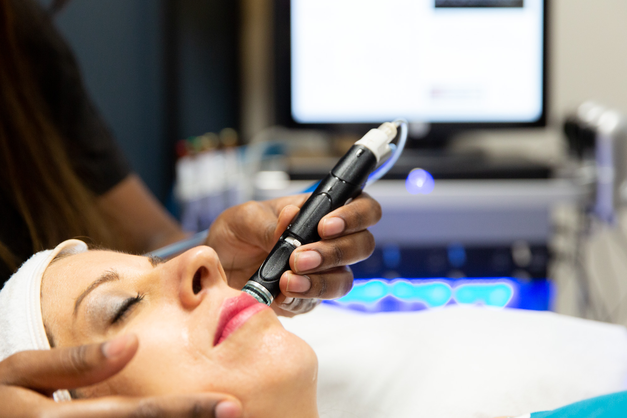 A Marcos Medical provider applies a vacuum-based abrasion tool to a woman's face during her HydraFacial. The woman is laying down with her eyes closed.