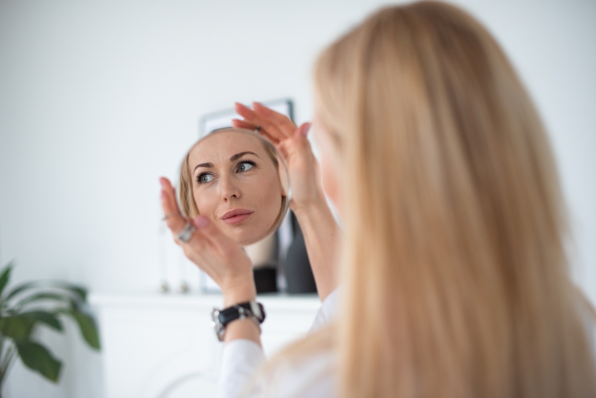 A beautiful woman admiring her skin in a mirror after having Laser Skin Resurfacing in San Antonio