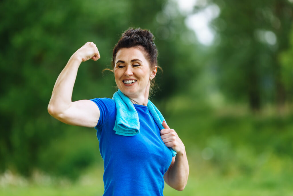 Smiling mature woman in a park showing off her bicep after toning muscles in San Antonio