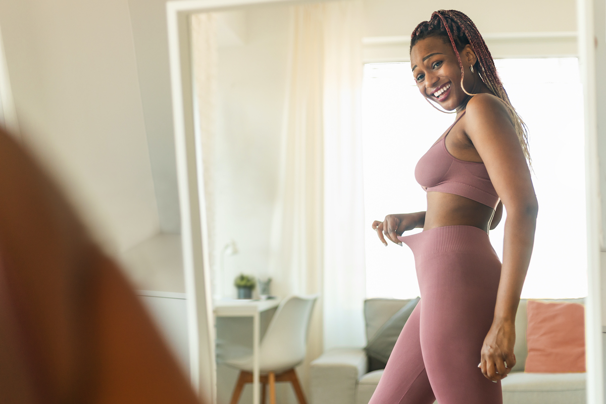 Fit black lady in front of mirror checking training and dieting results, looking at herself and smiling after semaglutide in San Andtonio