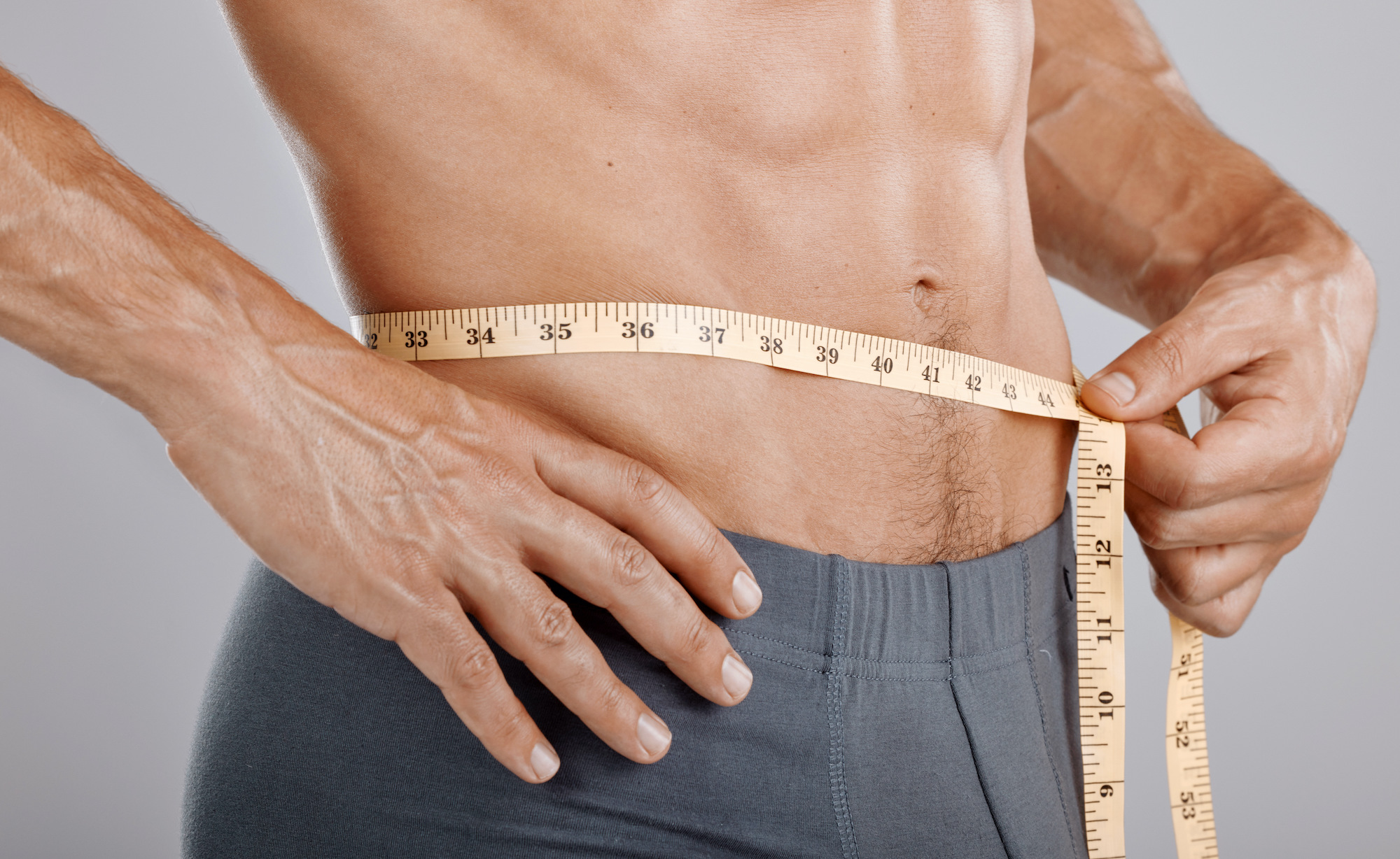 Man, body and tape measure on waist in studio on gray background while having weight loss management in San Antonio.