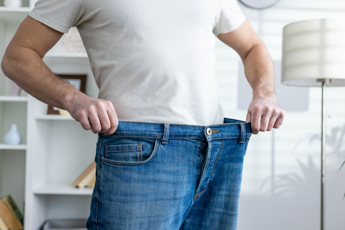 Man showing weight loss after having semaglutide in San Antonio by wearing loose jeans in a bright room