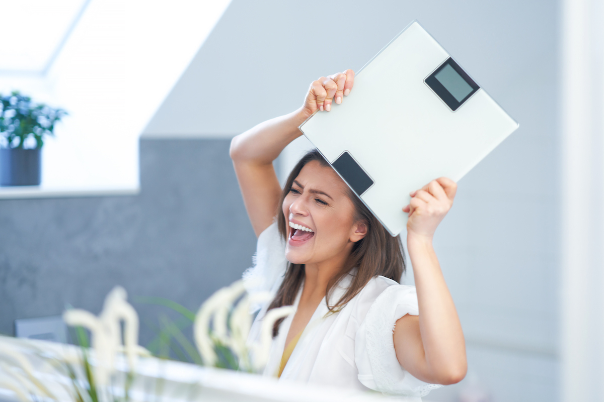 Young nice brunette woman in the bathroom with weight scale smiling and happy after weight loss from tirzepatide in San Antonio